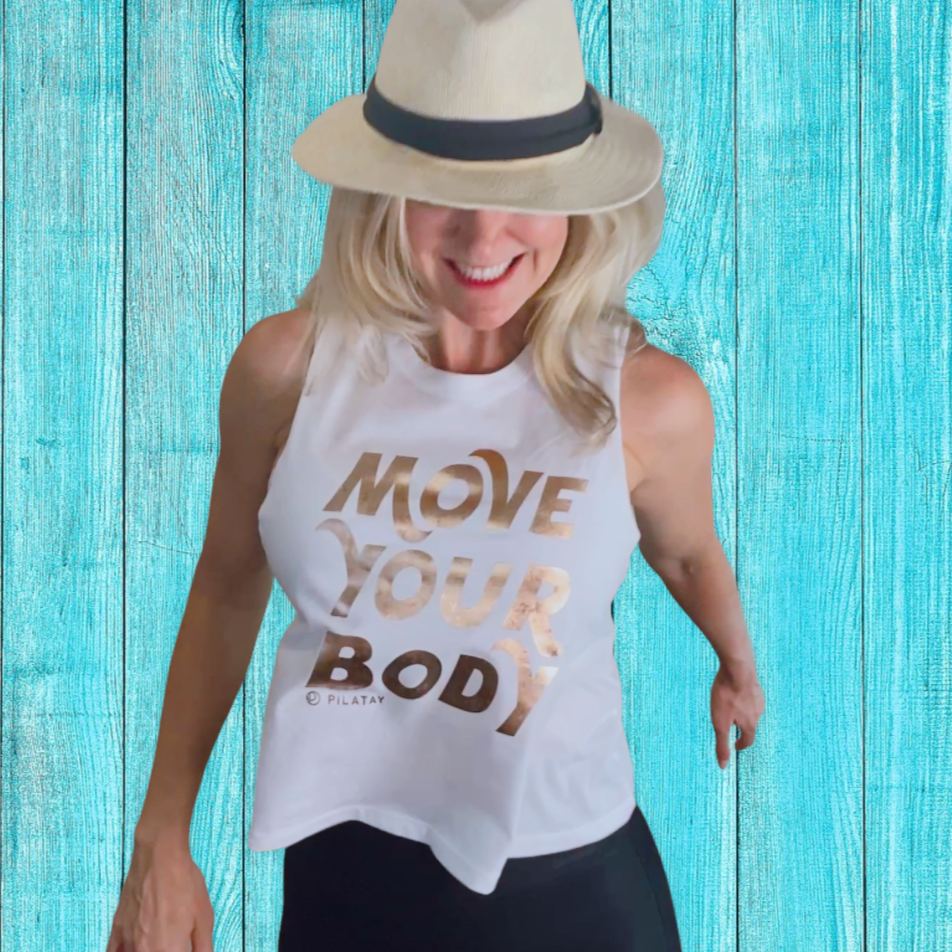 Girl jumping in a flowy white shirt with gold foil writing that says move your body - pilates shirt